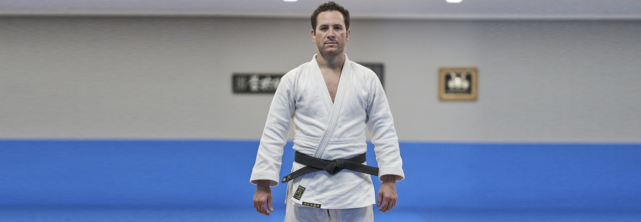 Tiago Camilo em pé com judogui e faixa preta em pé no tatame da academia